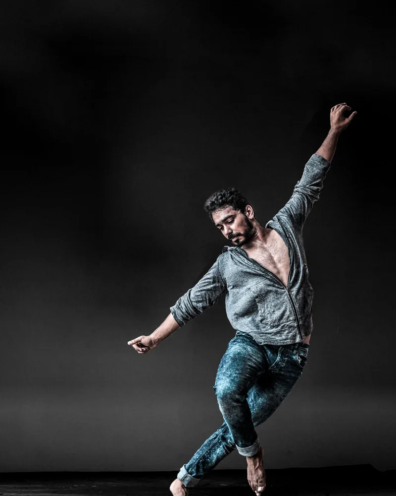 Persona en pleno movimiento de danza contemporánea sobre fondo oscuro, con el peso apoyado en un solo pie
